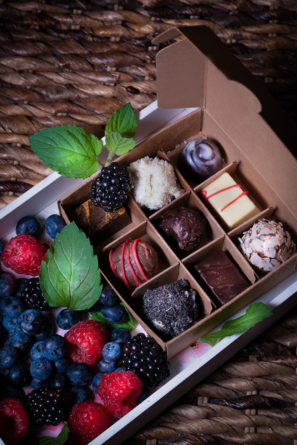 Foodfotografie. Luxury chocolate truffle box with fresh berries and mint leaves on woven texture background.