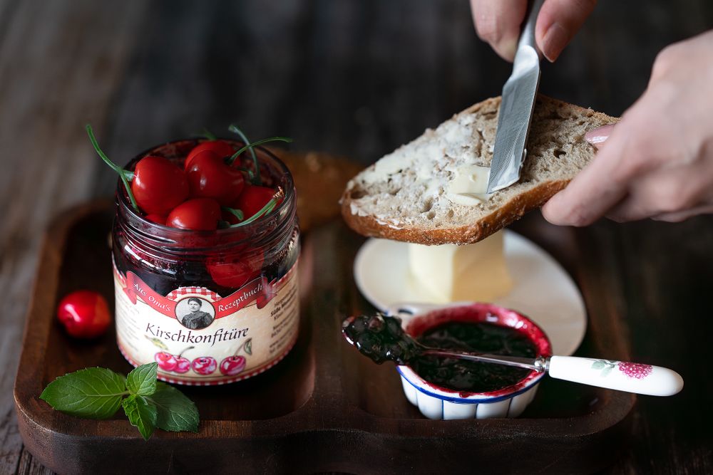 Foodfotografie. Cherry jam in jar with bread and butter on wooden board.