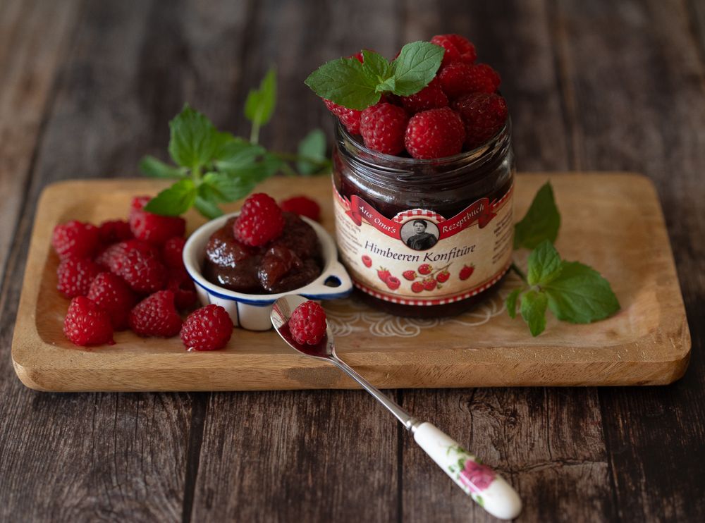 Foodfotografie. Raspberry marmelade with fresh berries and mint on wooden serving board.