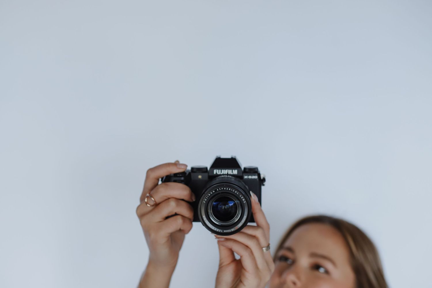 Photographer holding up Canon camera against light colored wall.