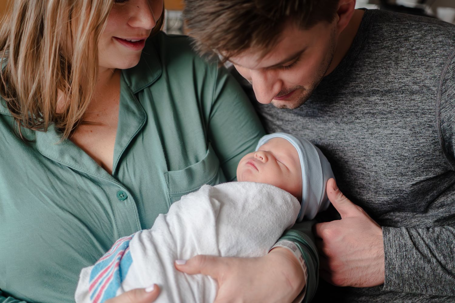 A couple gazes lovingly at their newborn baby wrapped in a white blanket.