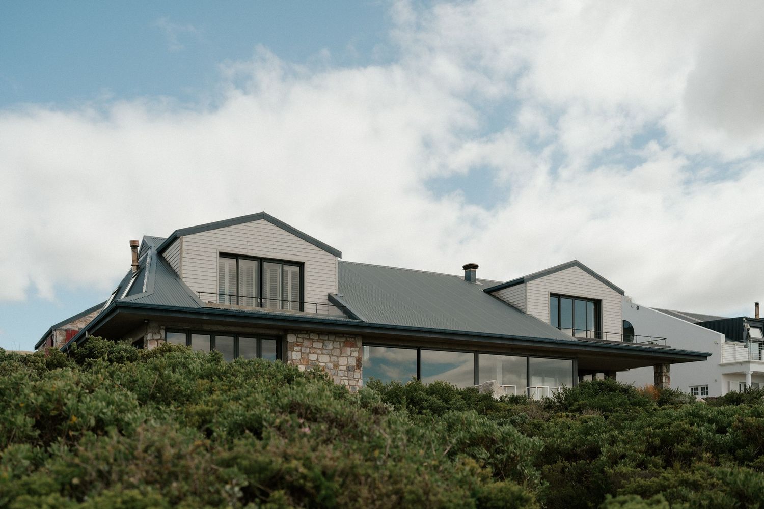 Modern mountain house with peaked roof and large windows against cloudy sky.