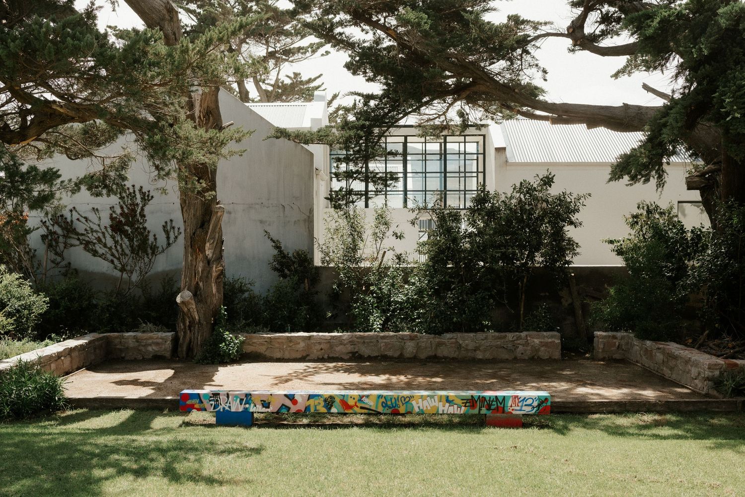 A white house exterior with trees and a painted decorative bench in the garden.