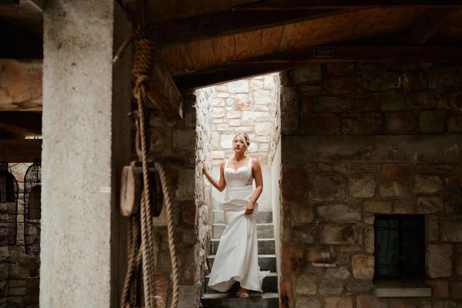 Person in a white wedding dress poses elegantly in a rustic stone archway at a historic venue.