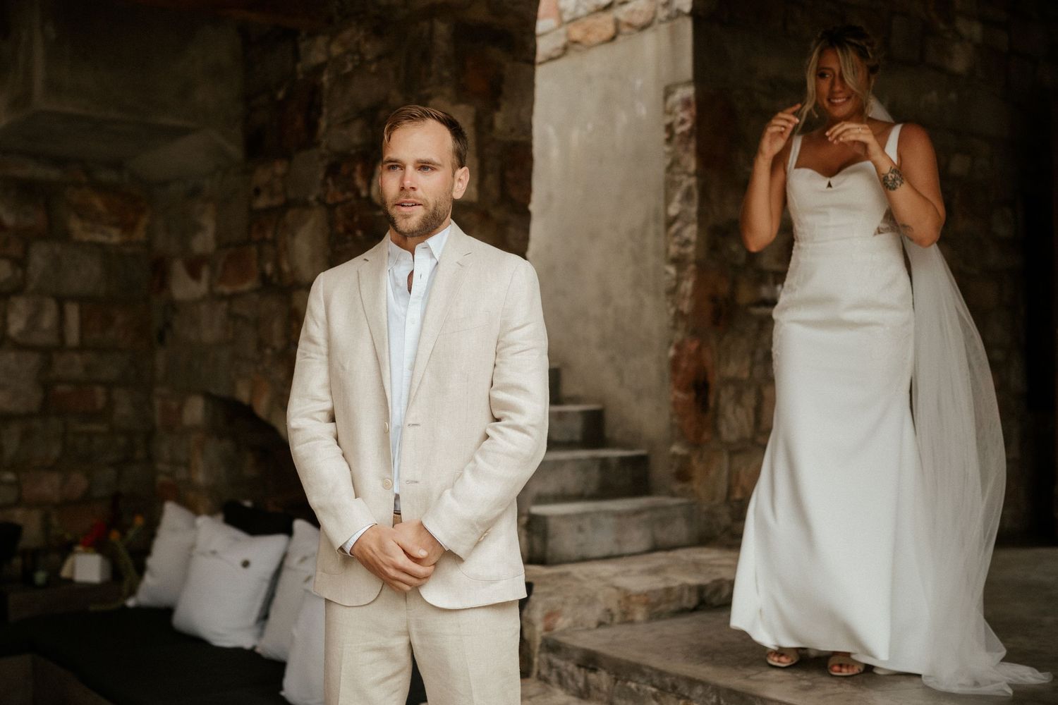 A first look wedding moment between newlyweds in a rustic stone setting with the bride in white and groom in beige.