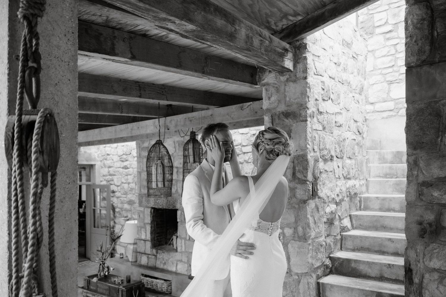 Two wedding dresses are displayed in a rustic stone-walled venue with wooden beams and vintage lanterns.