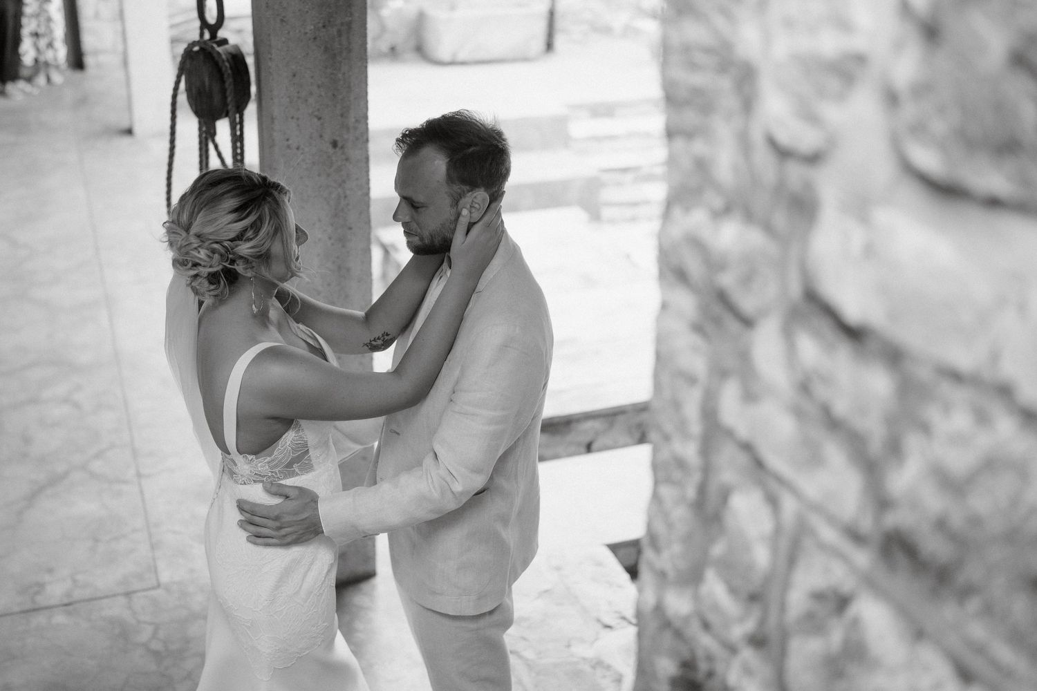 A romantic black and white wedding moment captured between a couple embracing in a stone archway.