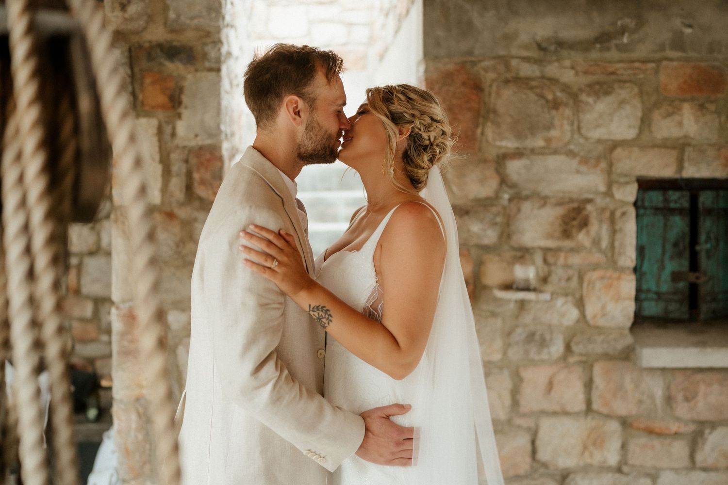 An intimate wedding portrait showing tender embrace between newlyweds against rustic stone architecture.