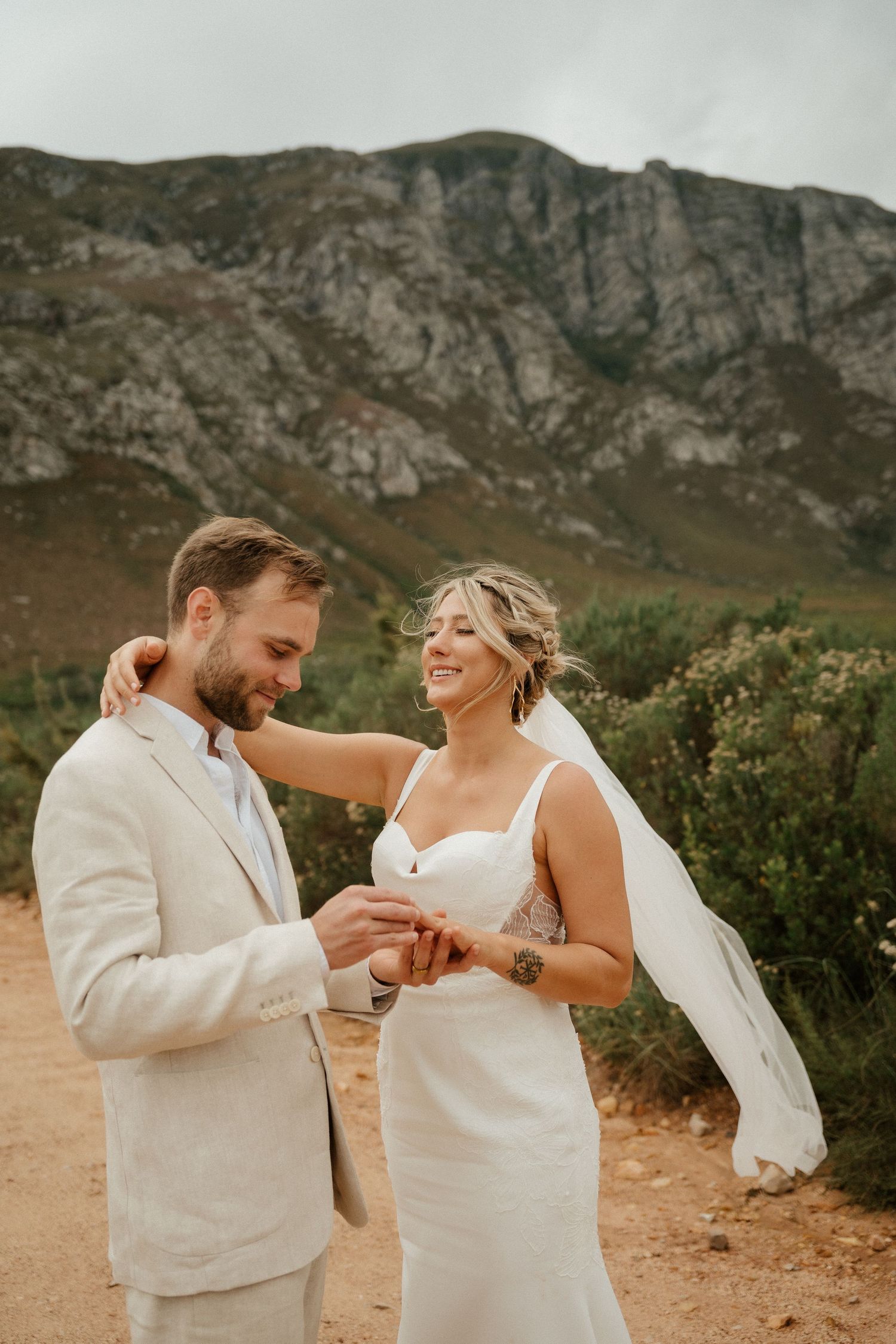 A romantic wedding moment with mountains in the backdrop as a couple shares a laugh while exchanging rings.