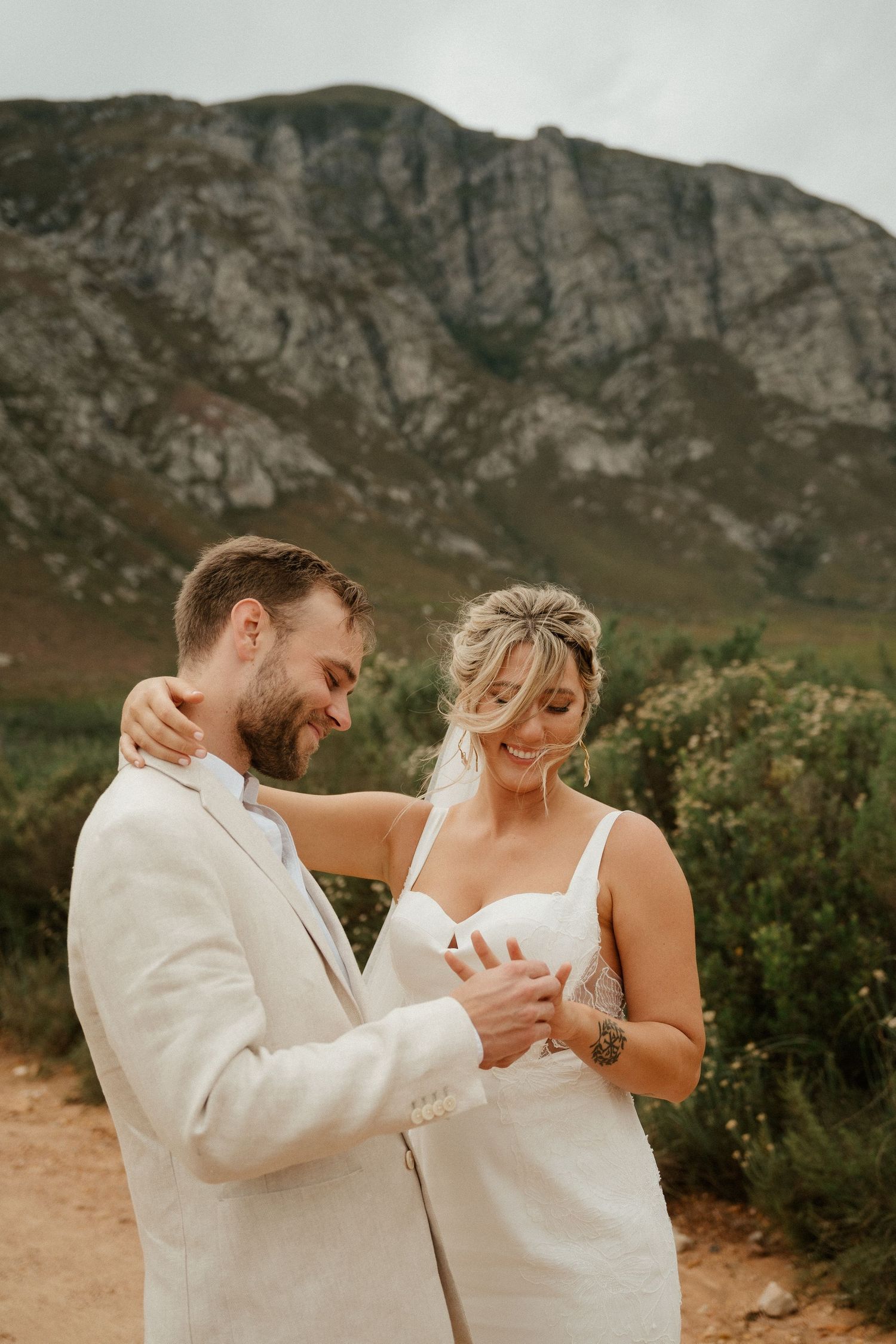 A romantic wedding moment captured against a dramatic mountainous backdrop on a dirt path.