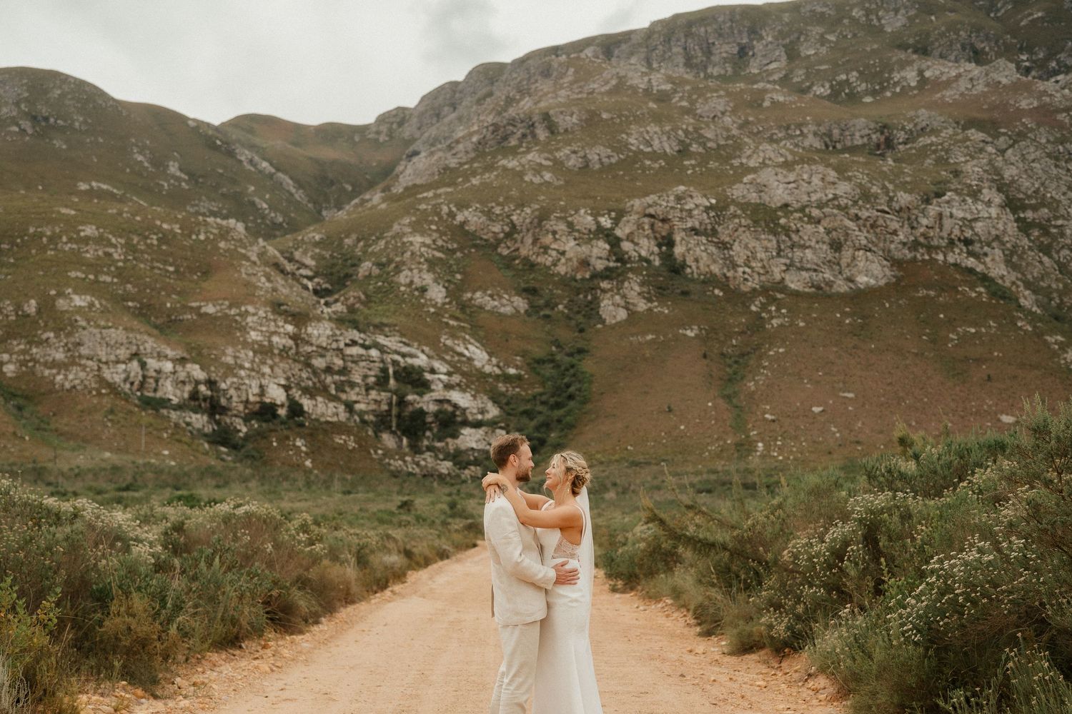 A romantic wedding photo on a mountain path with rugged cliffs in the background.
