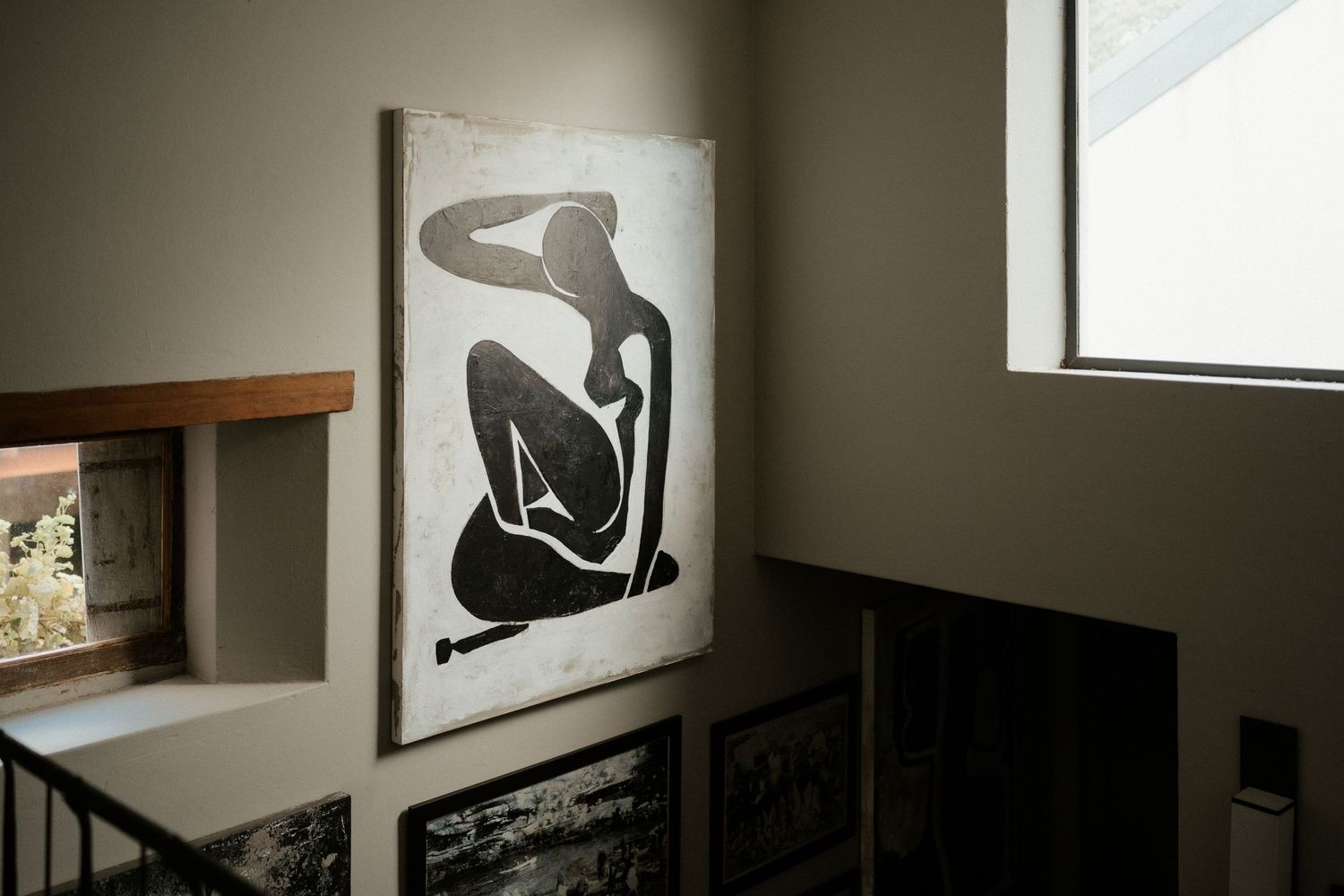 A minimalist black and white art print of a seated figure hangs on a modern interior wall.