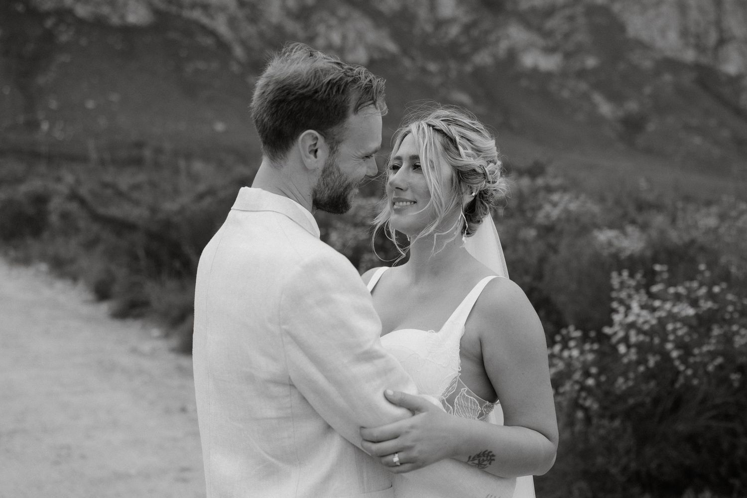A romantic black and white portrait of a wedding couple sharing an intimate moment against mountain landscape.