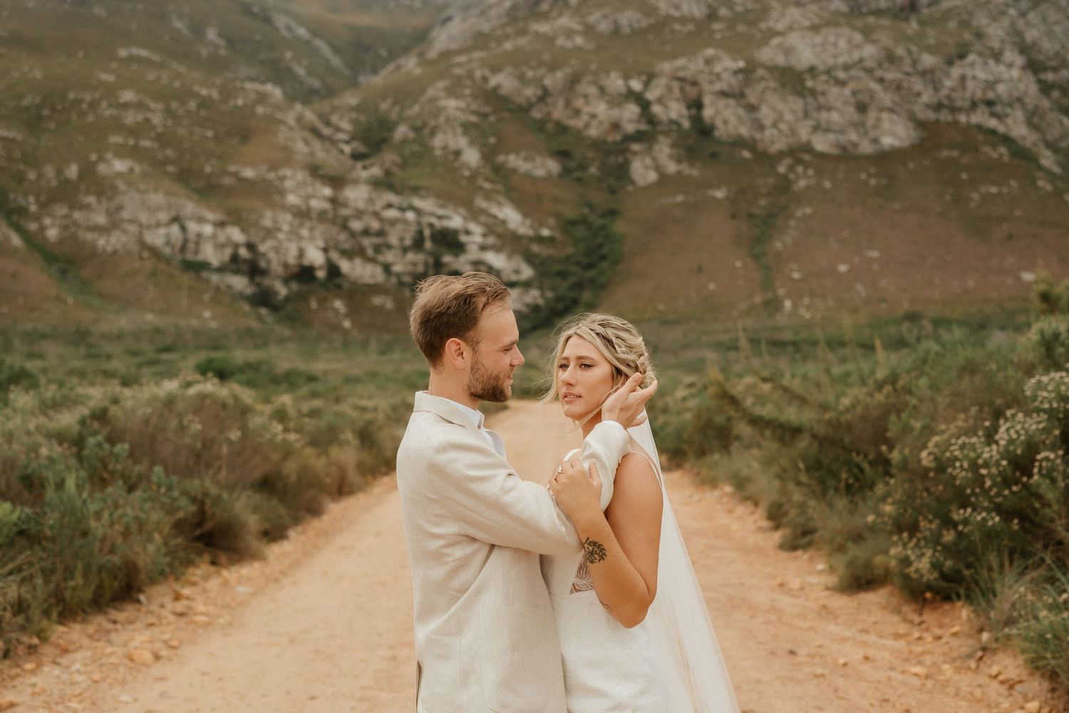 A tender moment between newlyweds on a dirt path surrounded by majestic mountains and golden light.