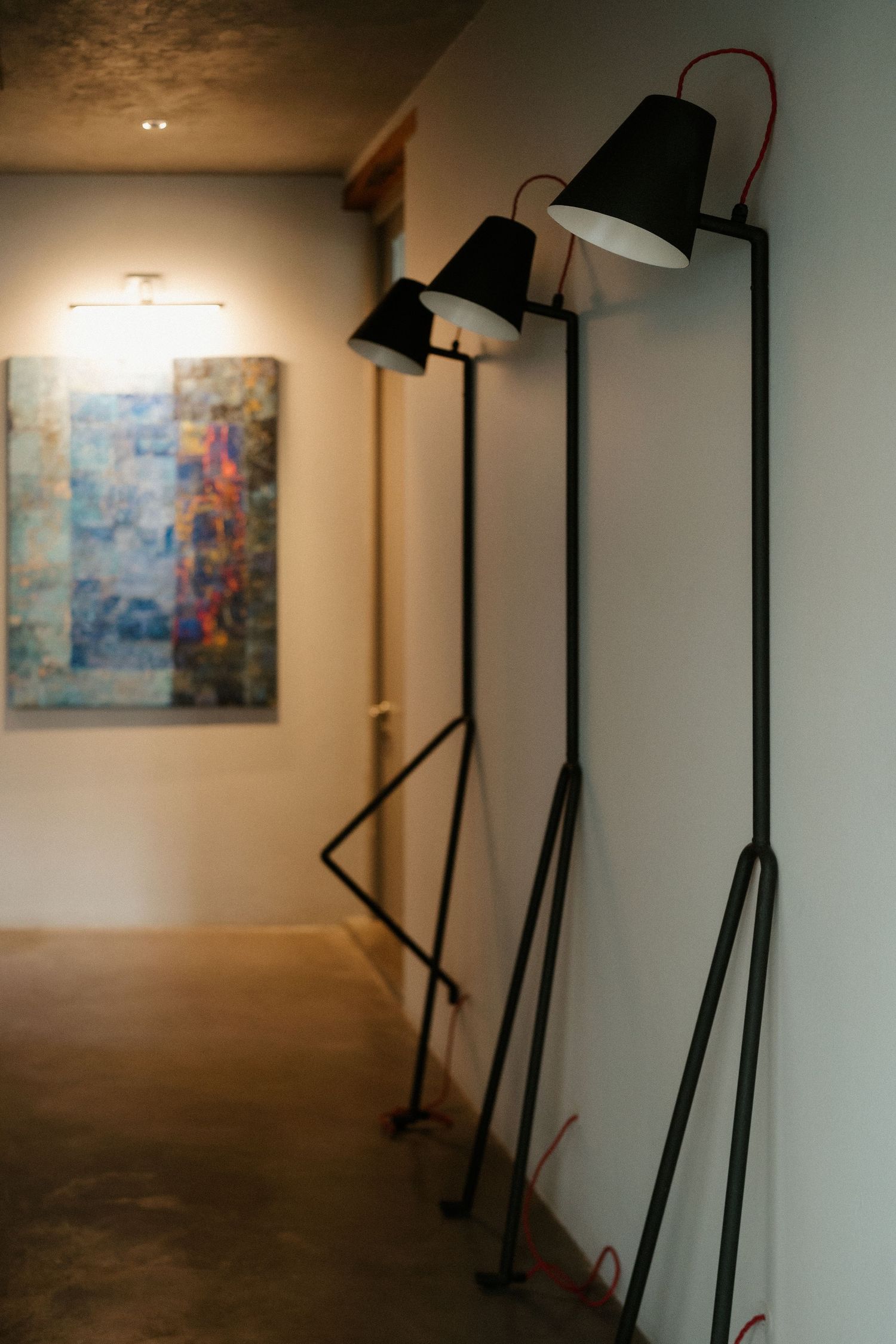 Modern black floor lamps line a hallway wall with abstract artwork in the background creating moody interior lighting.
