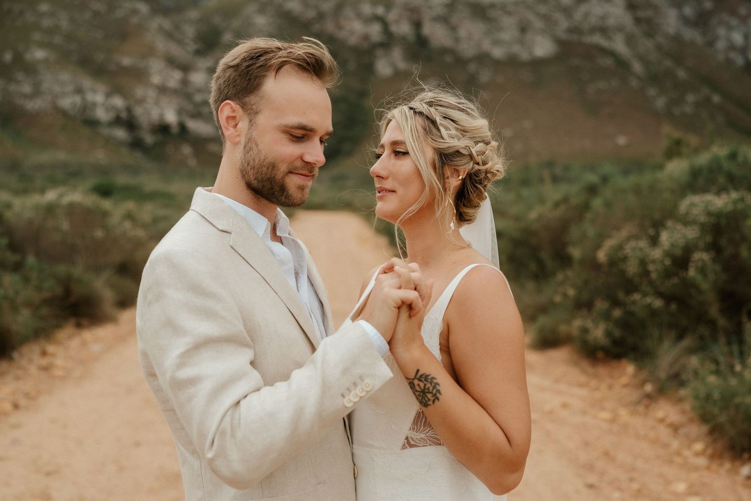 Romantic wedding portrait of a couple in light attire sharing an intimate moment on a mountain path.