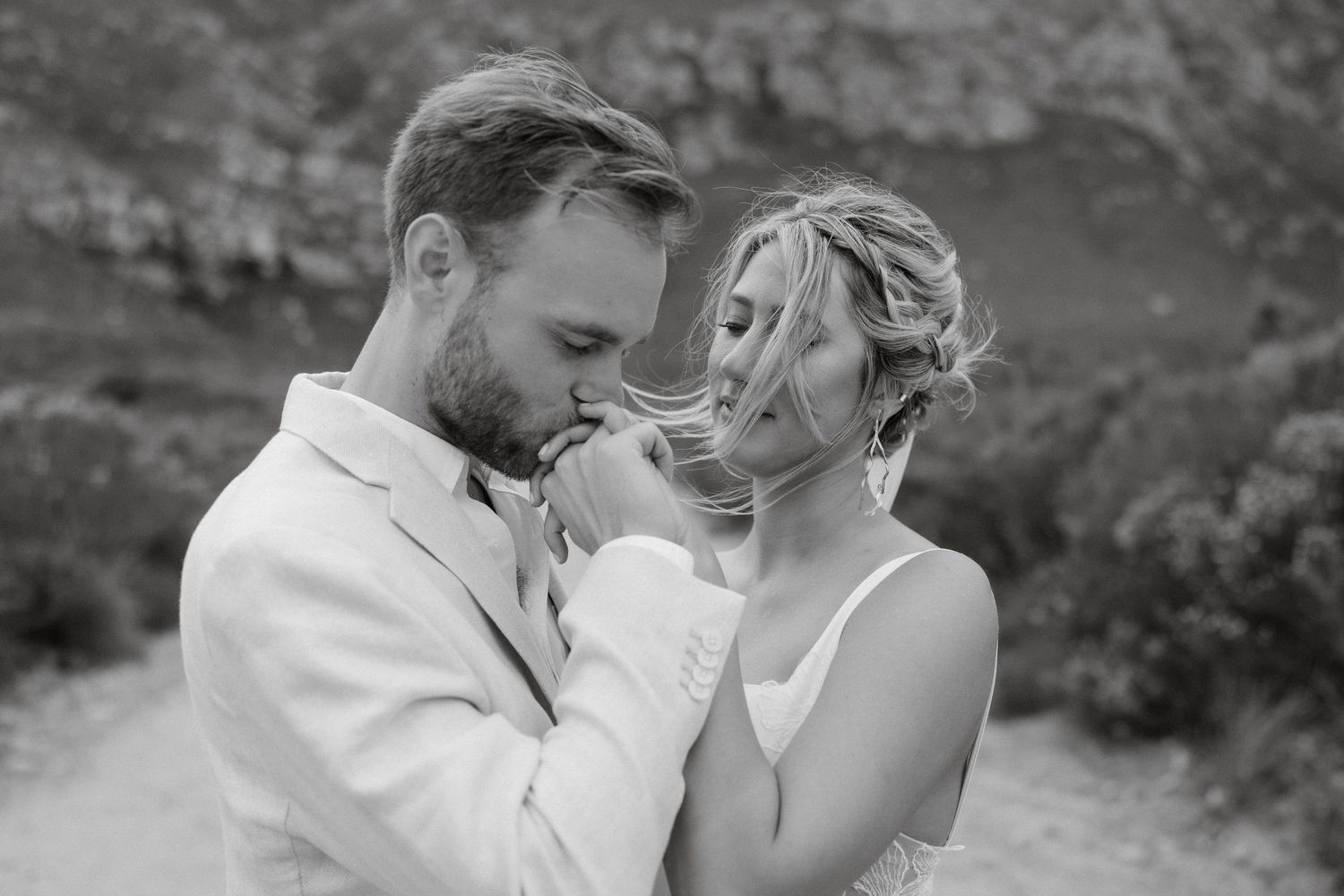 An intimate black and white portrait of a wedding couple sharing a tender moment outdoors.