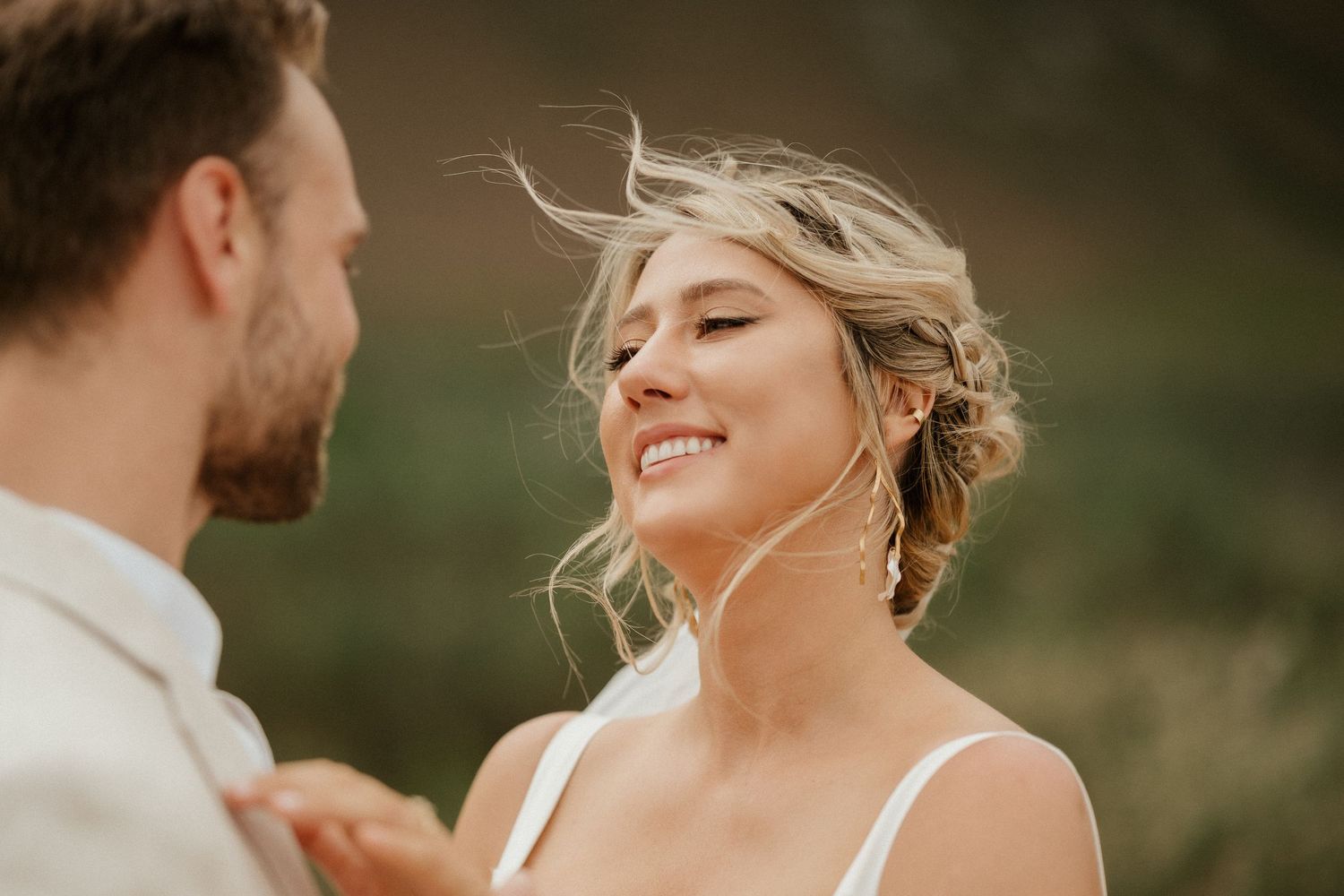 Tender wedding moment captured with golden light and windswept hair against natural scenery.