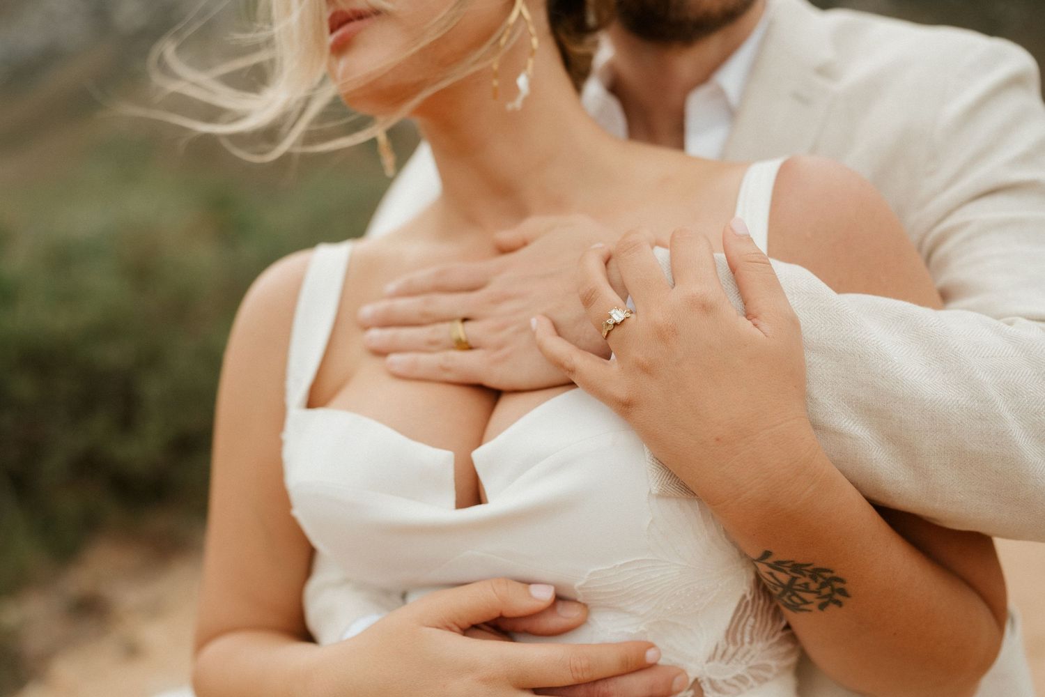 Close-up shot of hands with wedding rings embracing against a white dress.