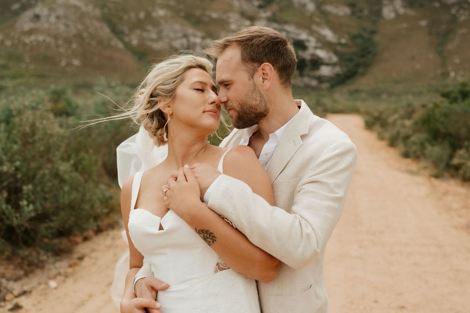 A tender romantic moment captured on a mountain path with dramatic natural landscape behind.