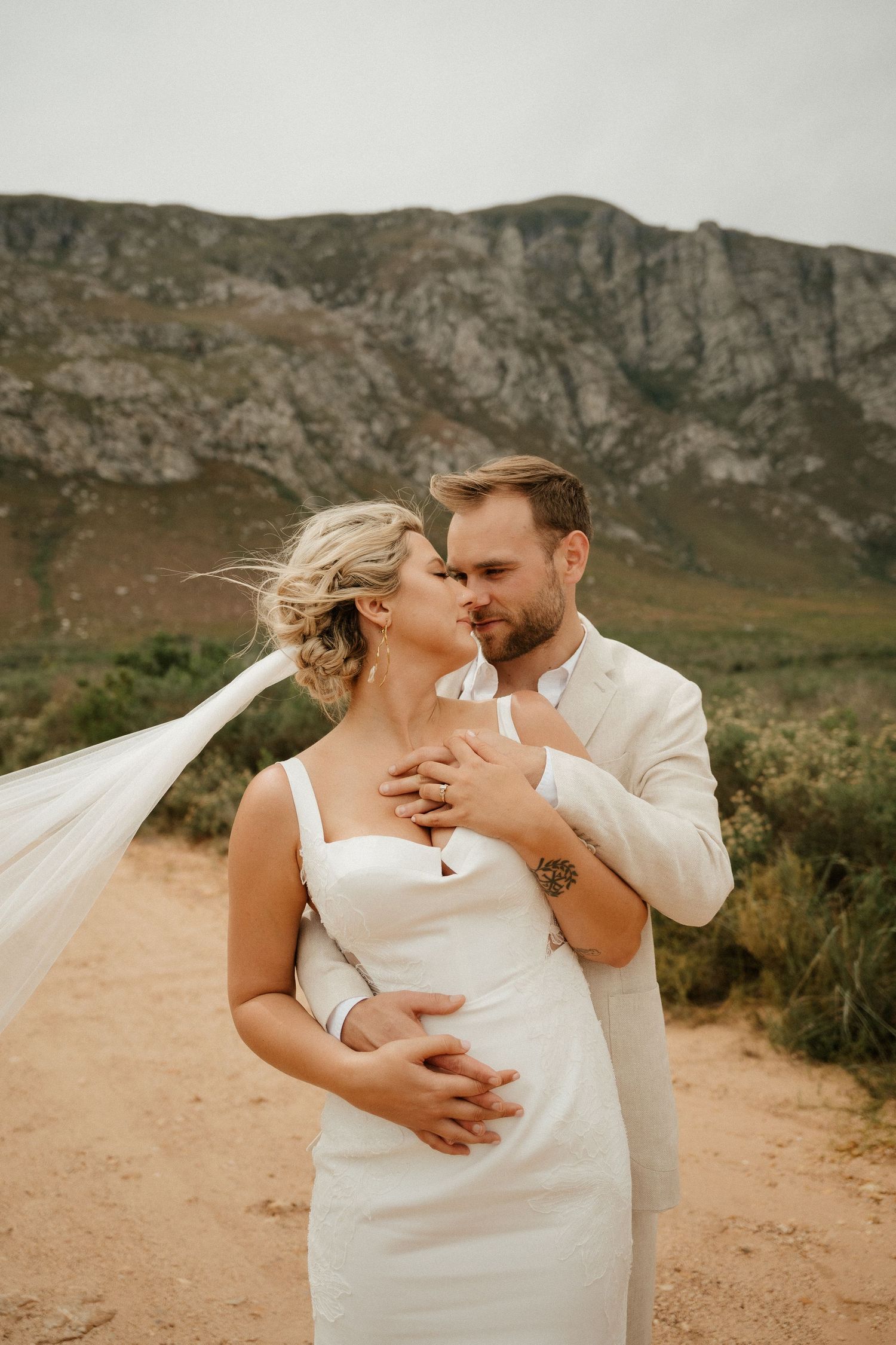 Intimate wedding portrait with flowing veil against majestic mountain backdrop.