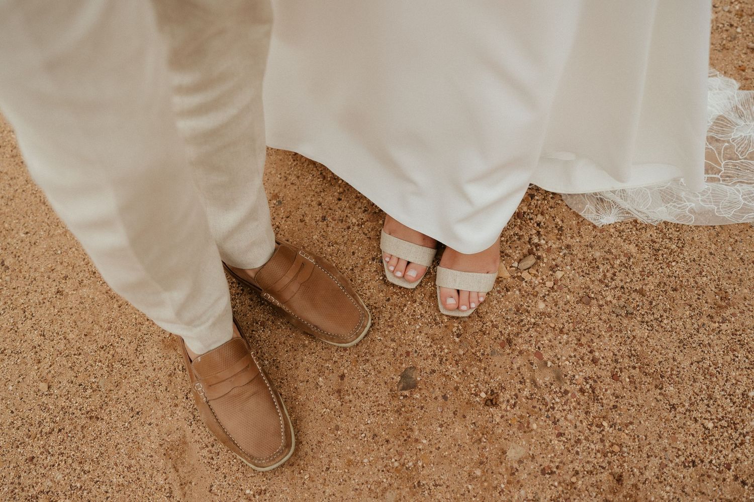 Detail shot of wedding footwear and dress hem on dusty ground.