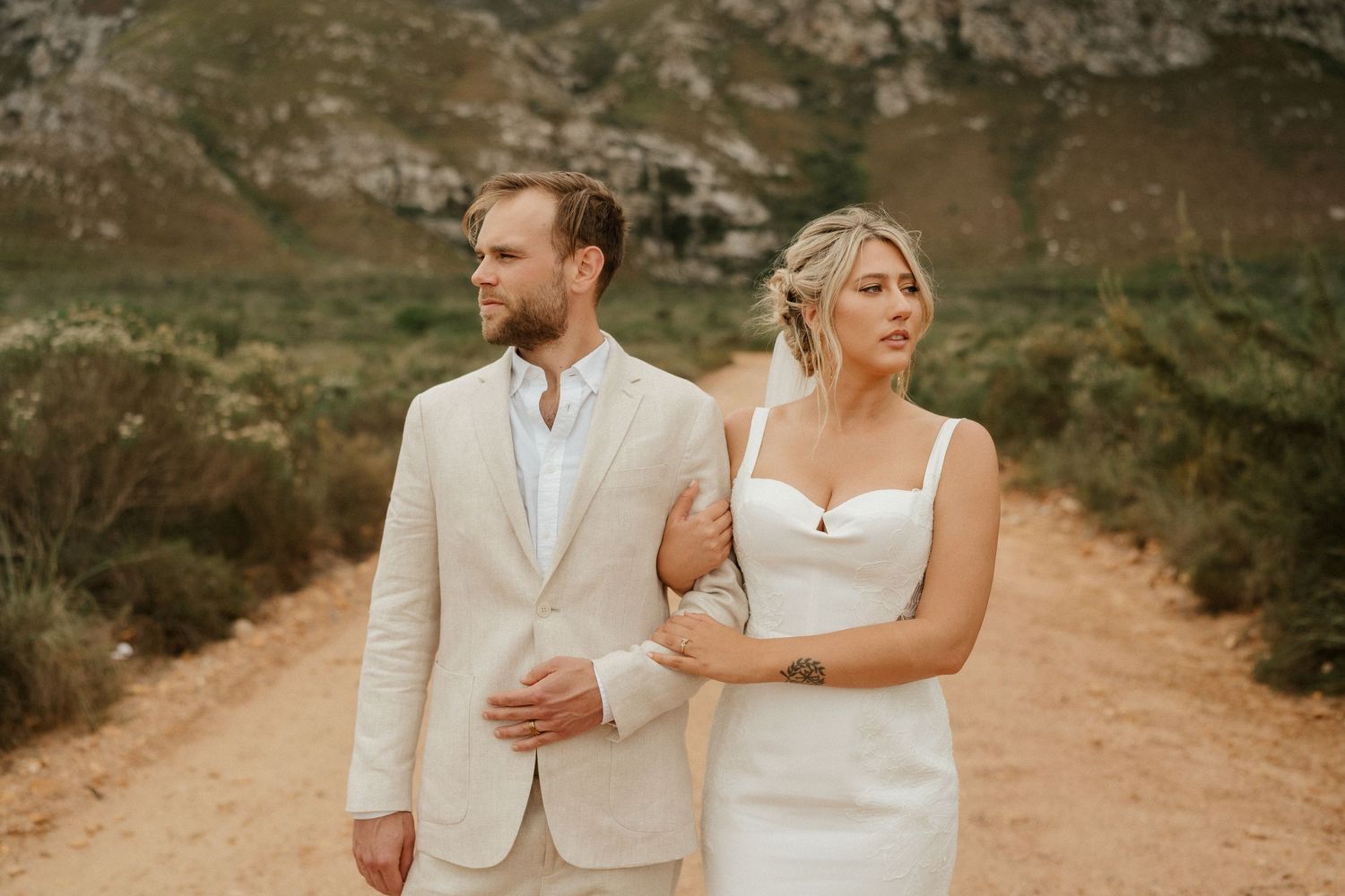 Elegant wedding portrait of a couple in cream and white attire standing on a rustic mountain path.