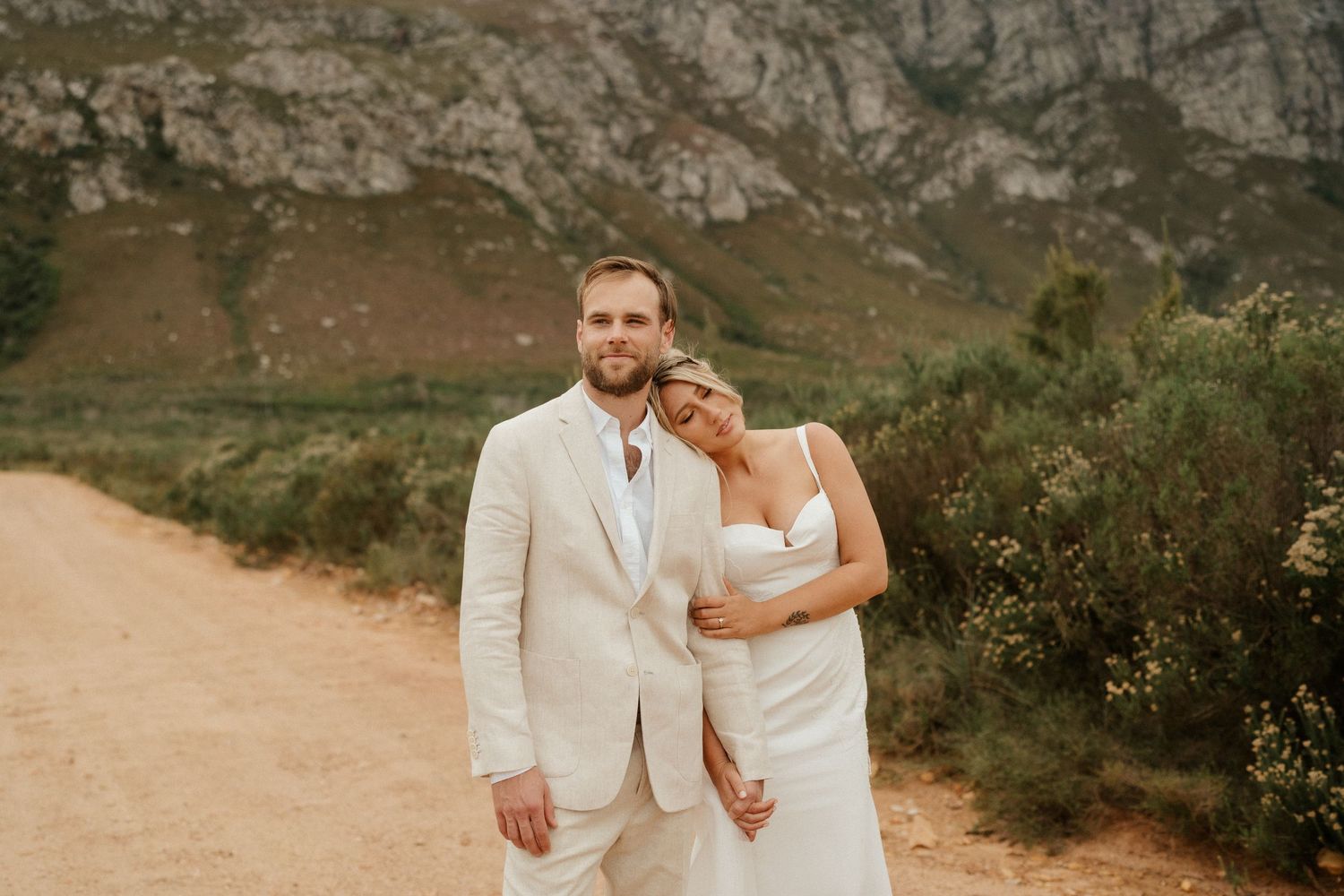 A romantic wedding portrait with rugged mountain scenery and a dirt path.