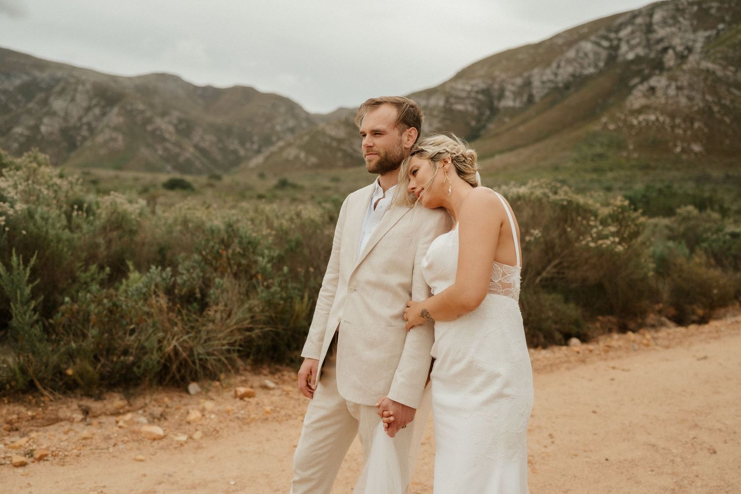 A romantic moment captured between newlyweds against a mountainous landscape at sunset.