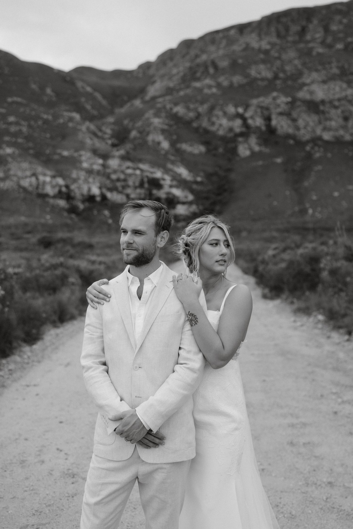 Black and white portrait of a couple in wedding attire on a mountain trail.