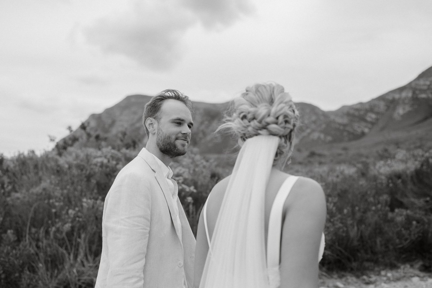 Black and white intimate wedding portrait with mountains and cloudy skies in the background.