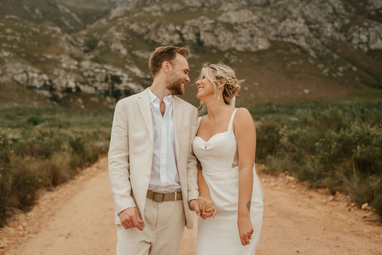 Romantic wedding couple in all white share a tender moment on mountain path.