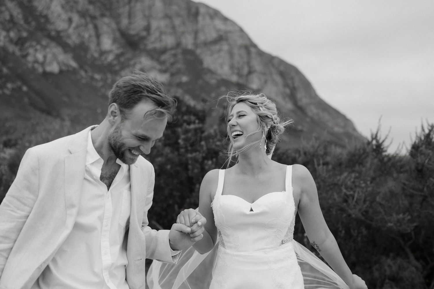 Black and white photo of a happy couple laughing together with mountains in background.