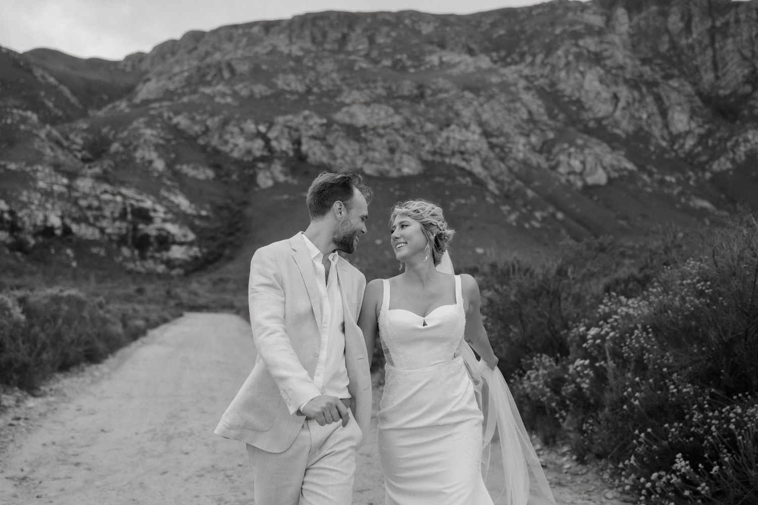 Black and white wedding portrait of couple walking along mountain trail.