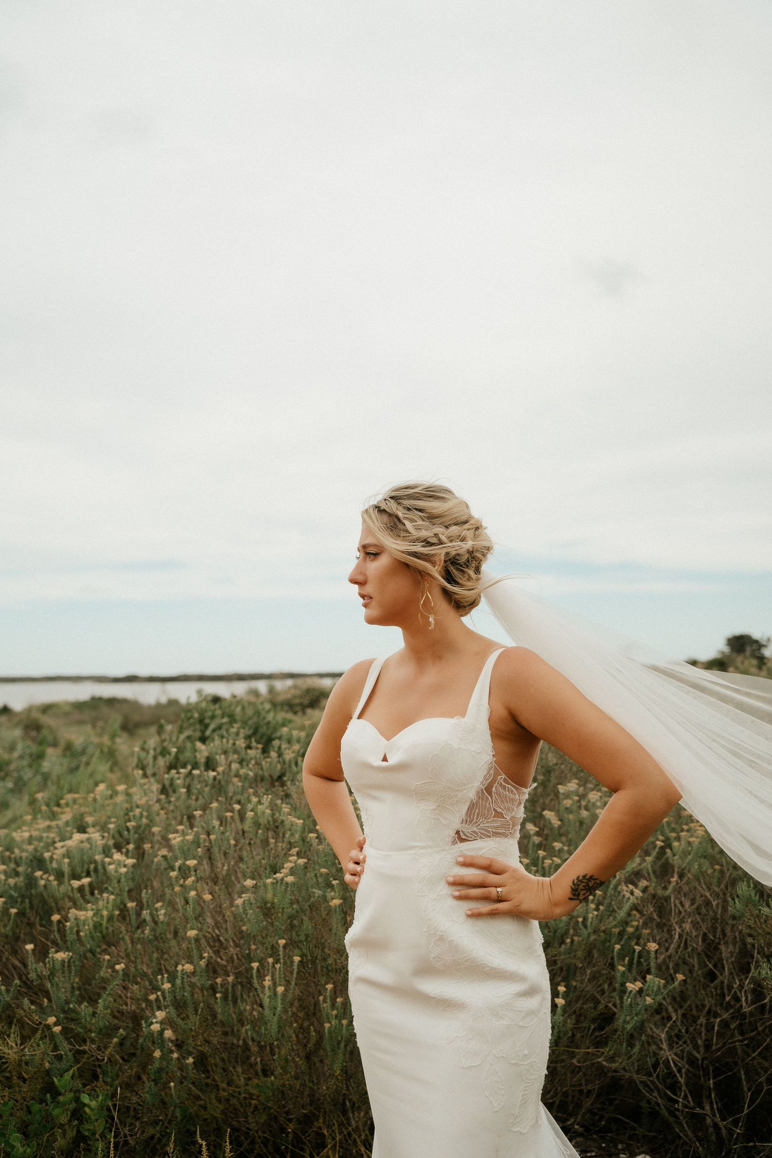 White wedding dress silhouetted against coastal landscape with wildflowers at sunset.