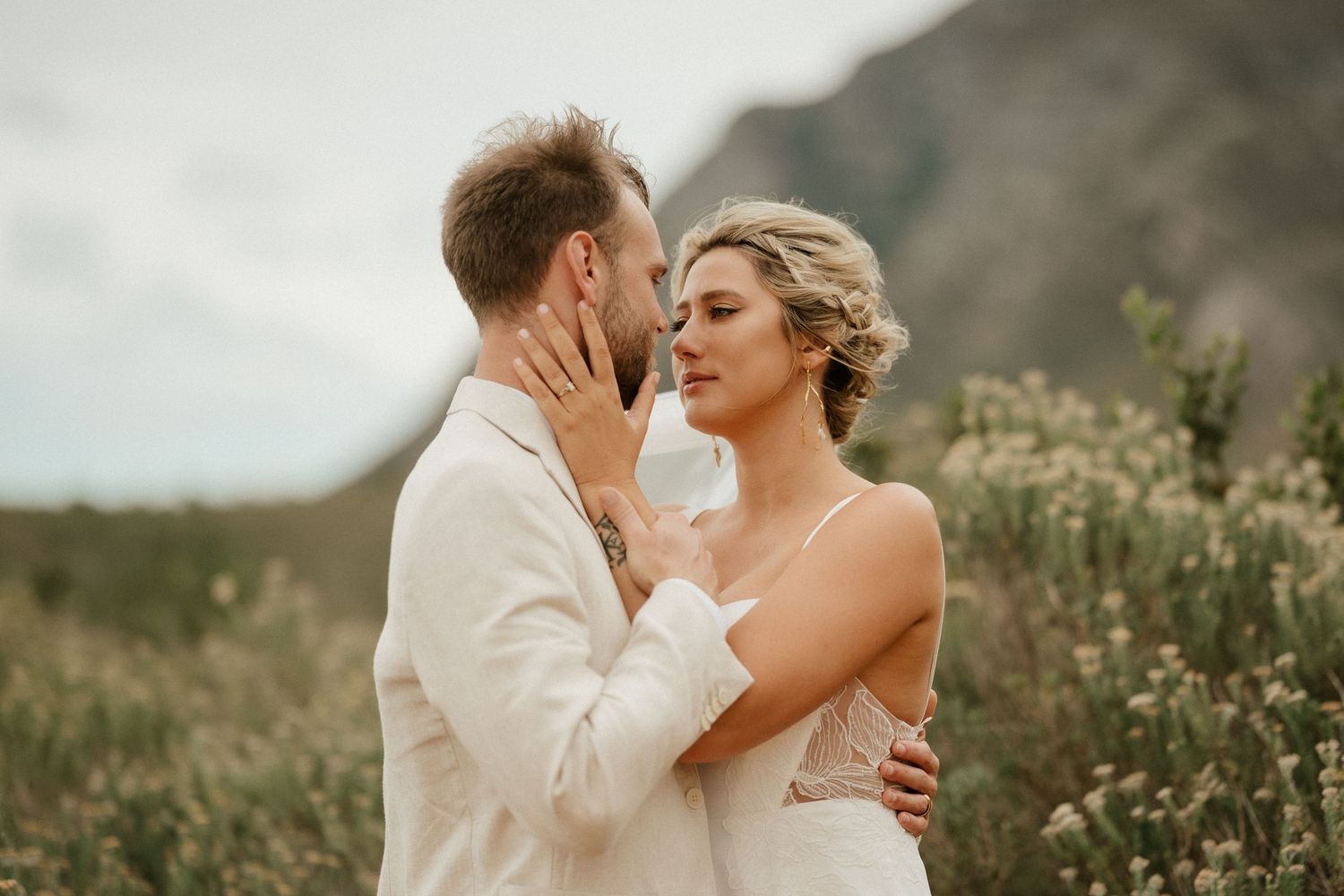An intimate moment shared between newlyweds with wild flowers and mountains creating a romantic backdrop.