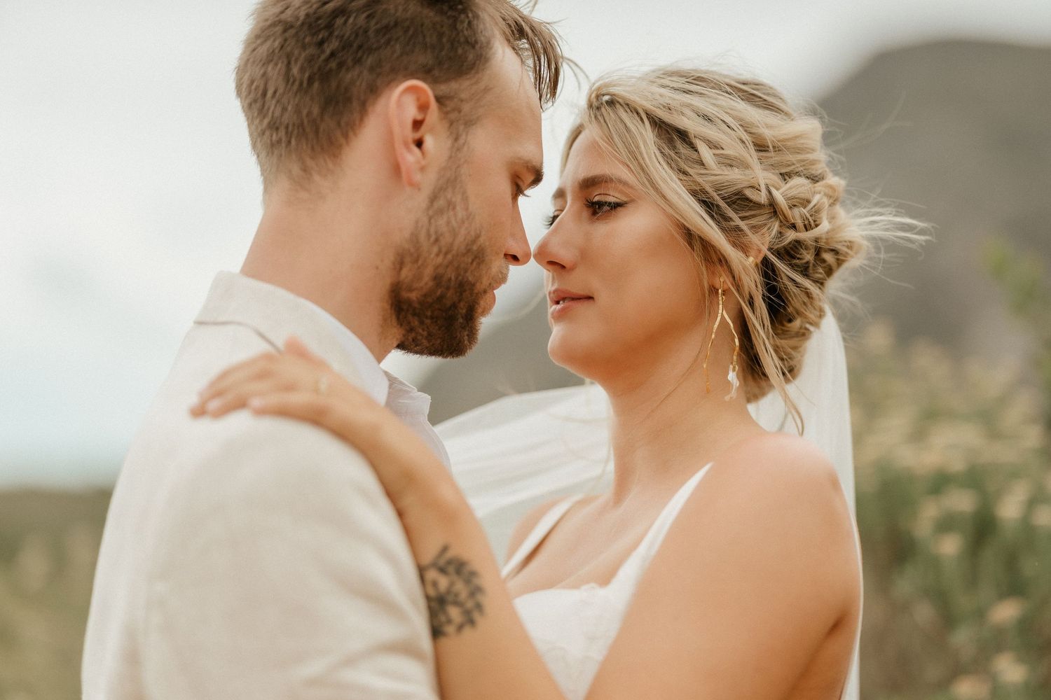 A romantic couple embraces in a sunlit meadow during their outdoor wedding ceremony on a warm summer day.