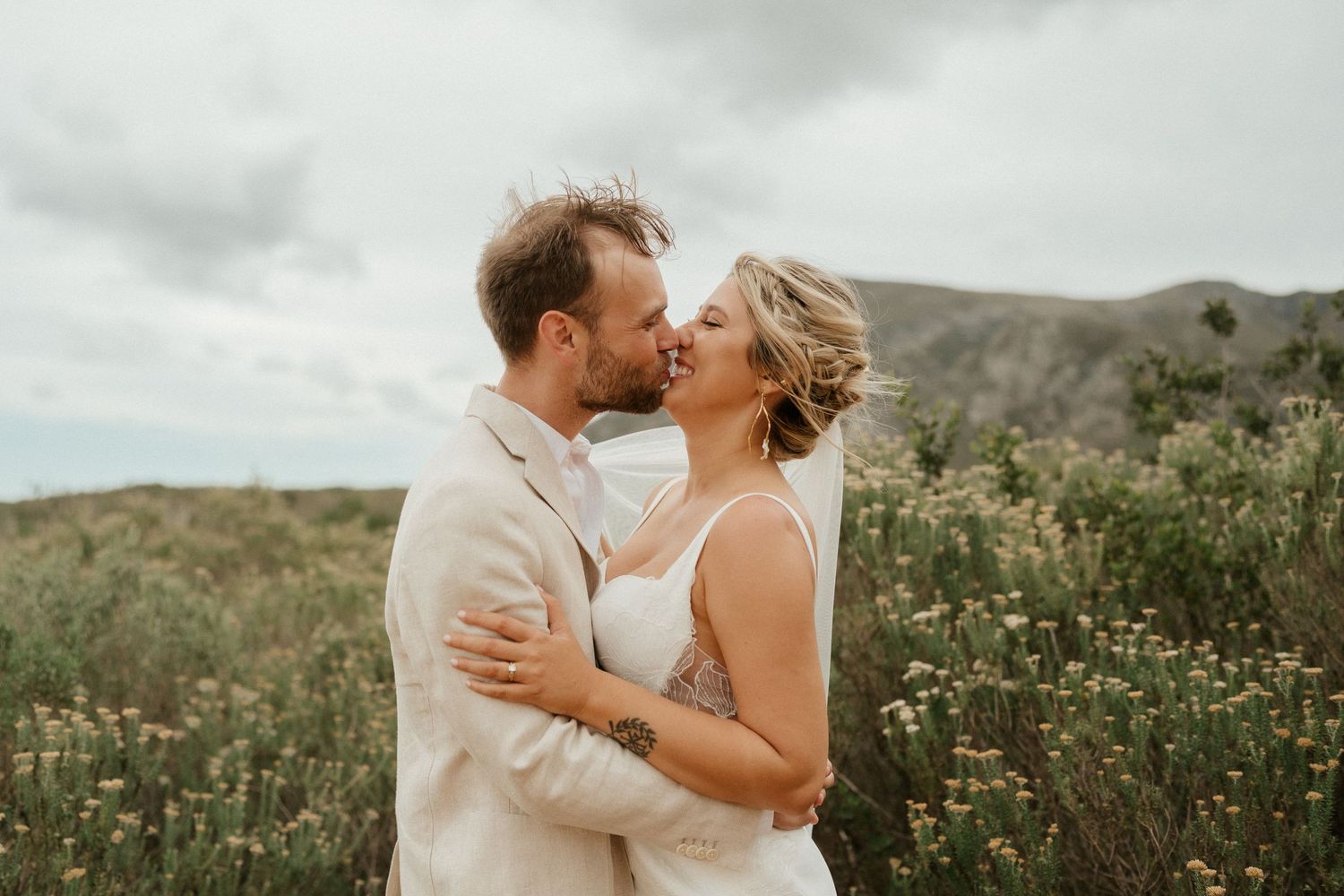 Embracing couple share a romantic moment against a backdrop of mountains and wildflowers.
