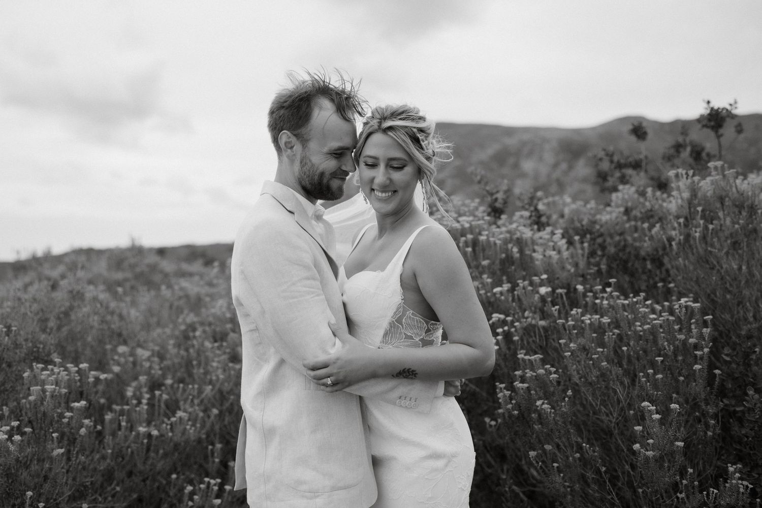 A romantic black and white photo of a couple embracing in a wildflower field.