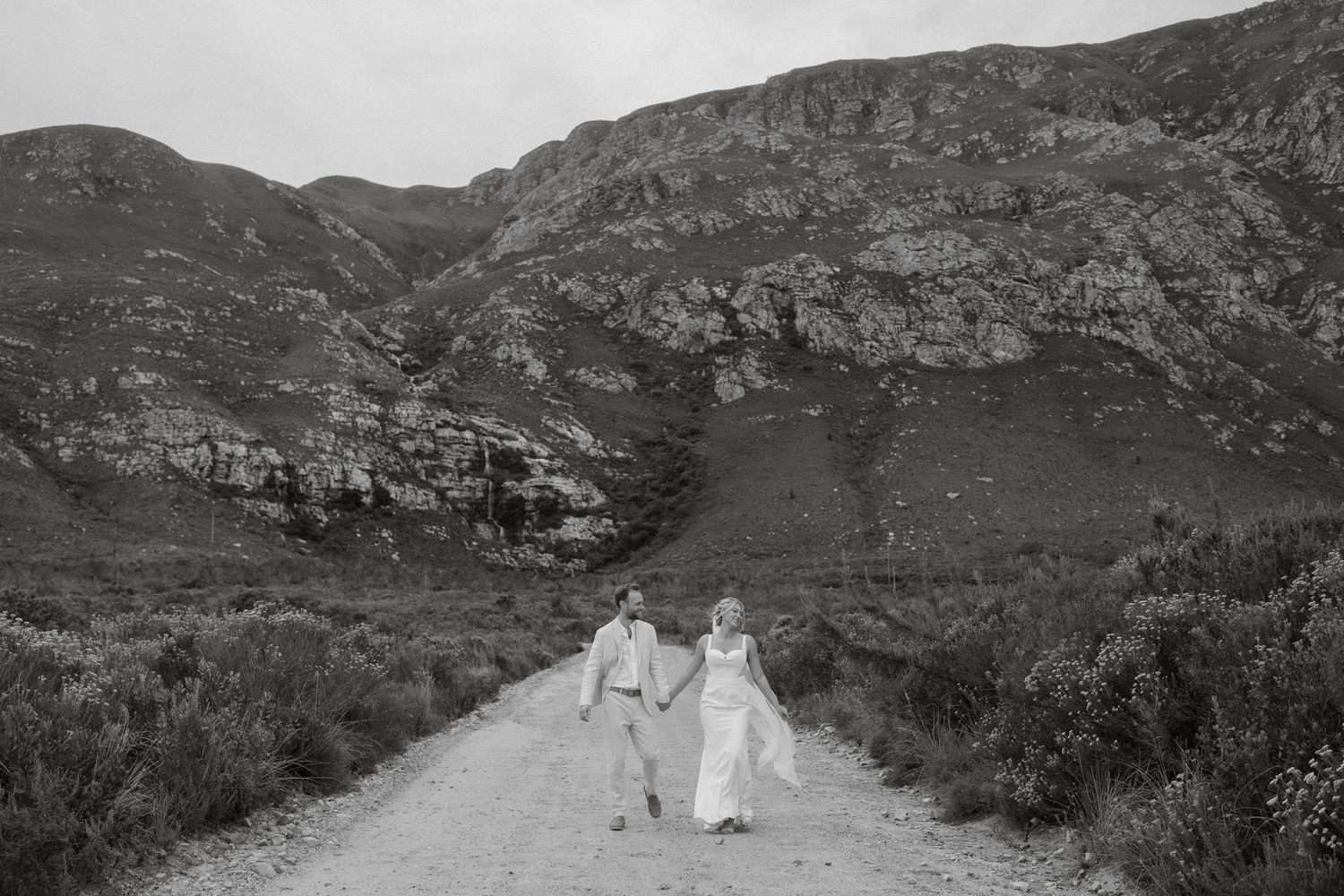 Wedding couple walking down mountain path together in black and white photography.
