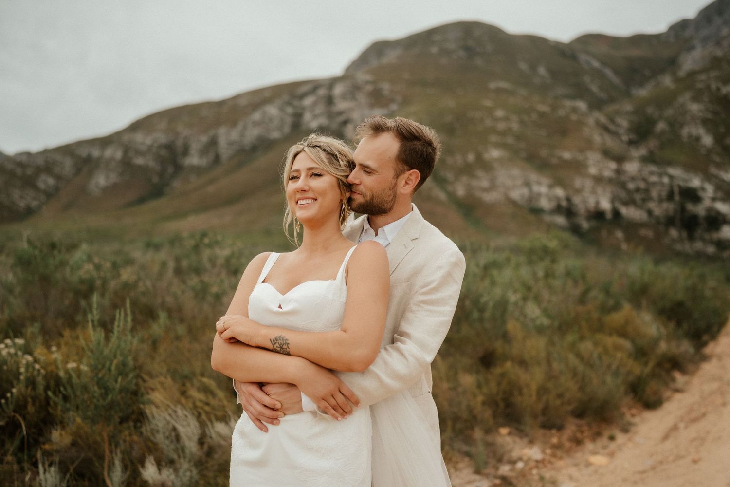 Intimate wedding portrait with couple embracing against mountainous backdrop.