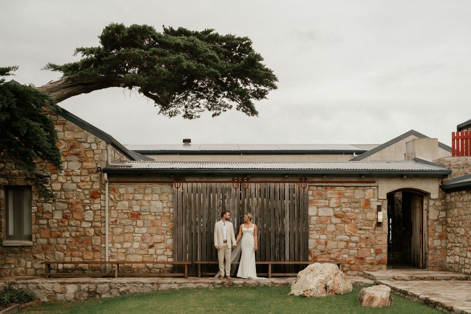 Rustic stone building with wooden gates and overhanging cypress tree creates vintage atmosphere.