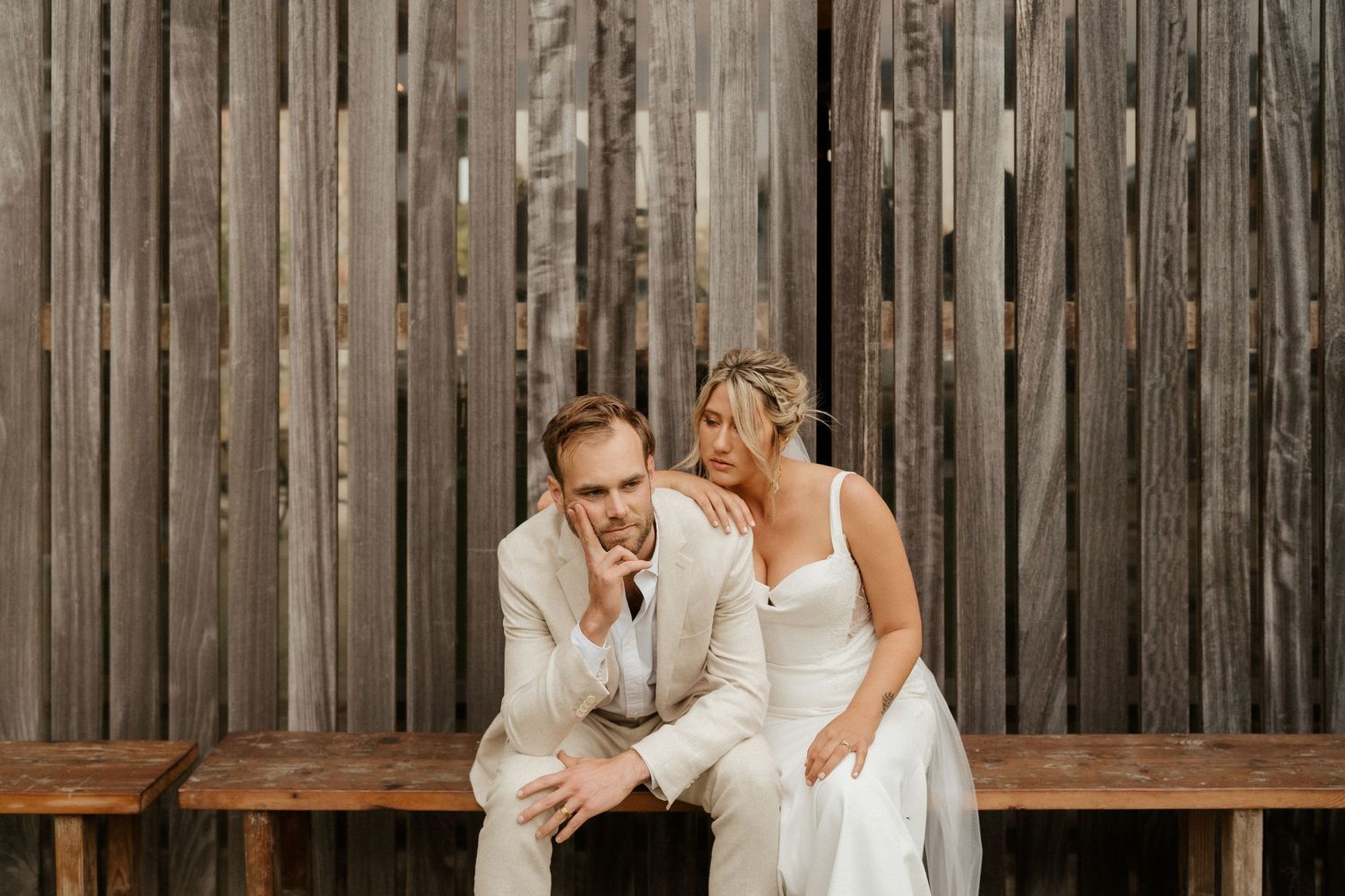 Couple sharing intimate moment on wooden bench against rustic fence.