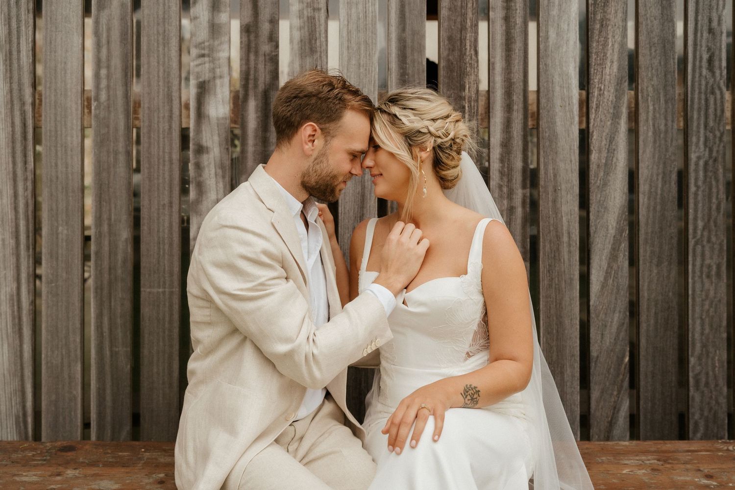 A romantic wedding moment between newlyweds sharing an intimate embrace against a rustic wooden fence backdrop.