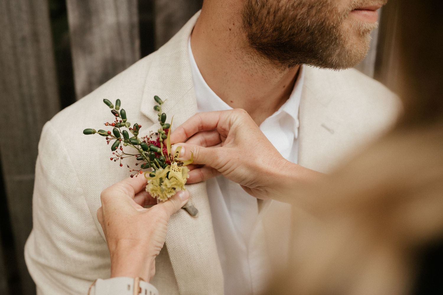 Someone pins a delicate floral boutonniere onto a white suit jacket.