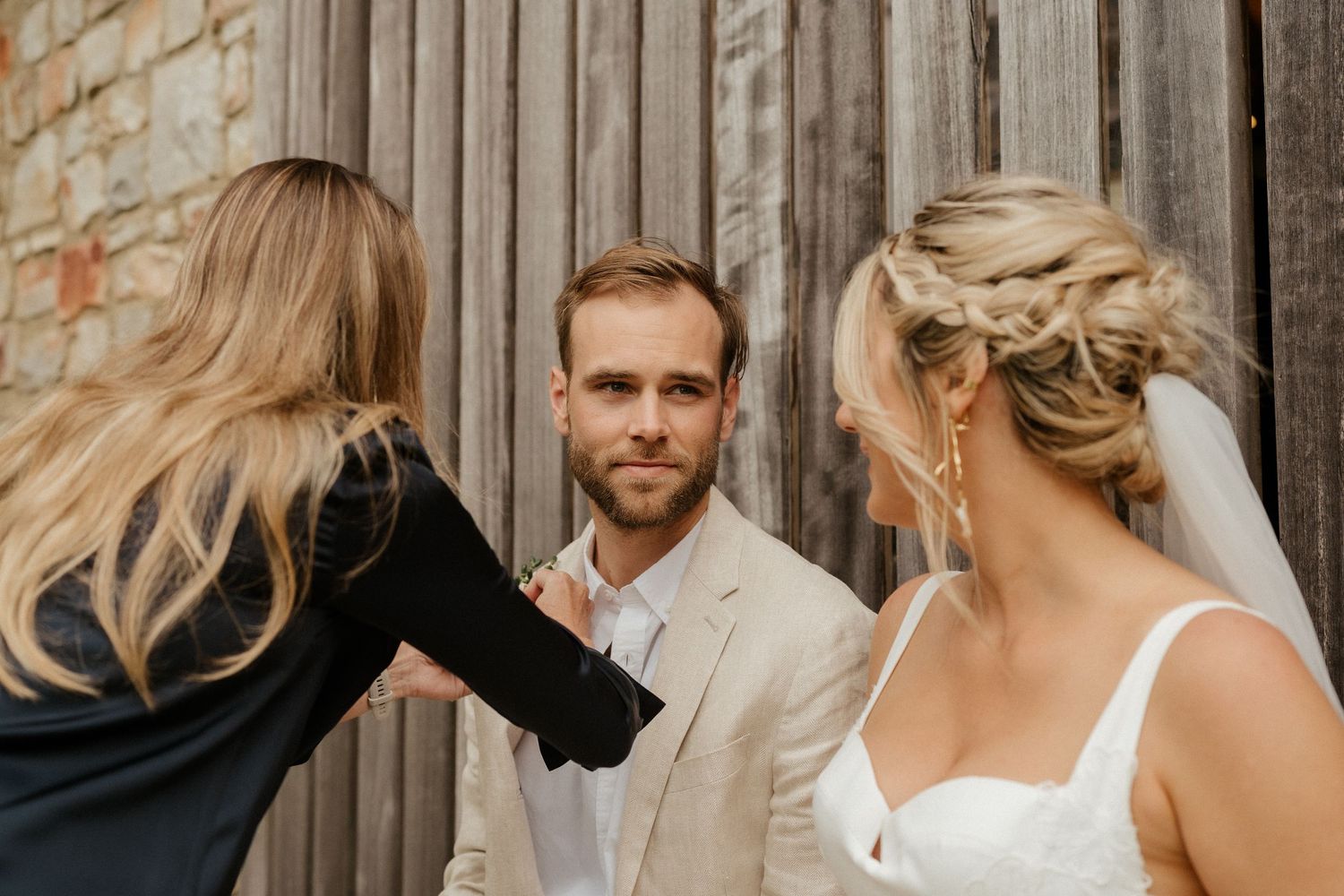 Wedding party gets ready for photos against rustic wooden wall on special day.