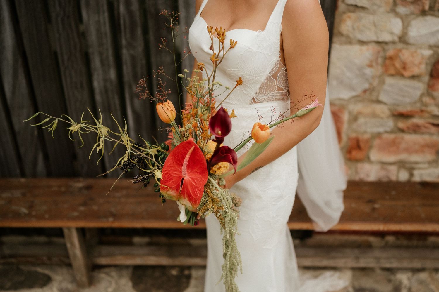 Elegant bridal bouquet with red flowers and greenery against rustic backdrop.