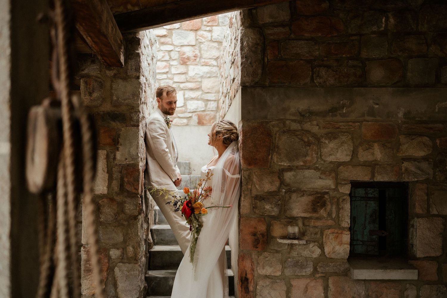 Wedding couple standing in stone archway with natural light streaming in.