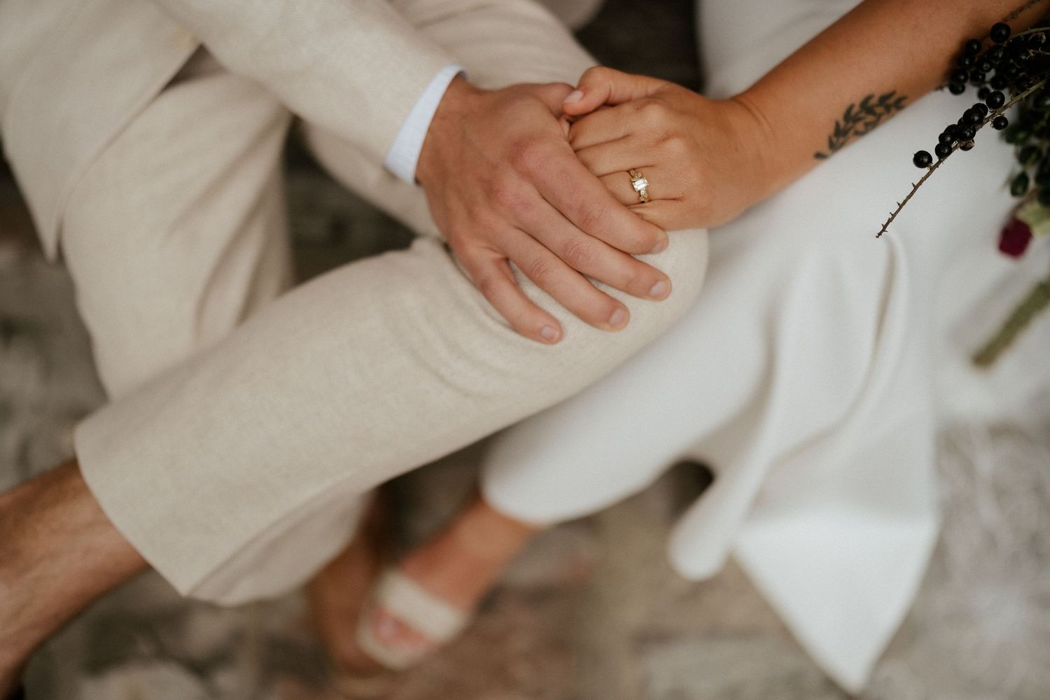 Close-up view of two hands wearing white attire and a wedding band touching gently.