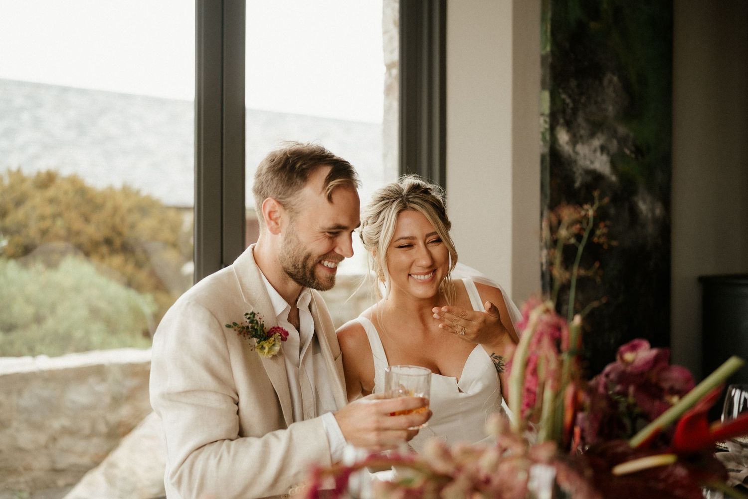 A couple shares a candid moment during their wedding reception by a window.